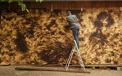 Georg Thumbach vor dem eigens für St. Wendel geschaffenen Triptychon (o. T., 2025, Stechbeitel und Schleifpapier auf gebrannten Grobspanplatten 278 x 621 cm)