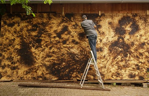 Georg Thumbach vor dem eigens für St. Wendel geschaffenen Triptychon (o. T., 2025, Stechbeitel und Schleifpapier auf gebrannten Grobspanplatten 278 x 621 cm)